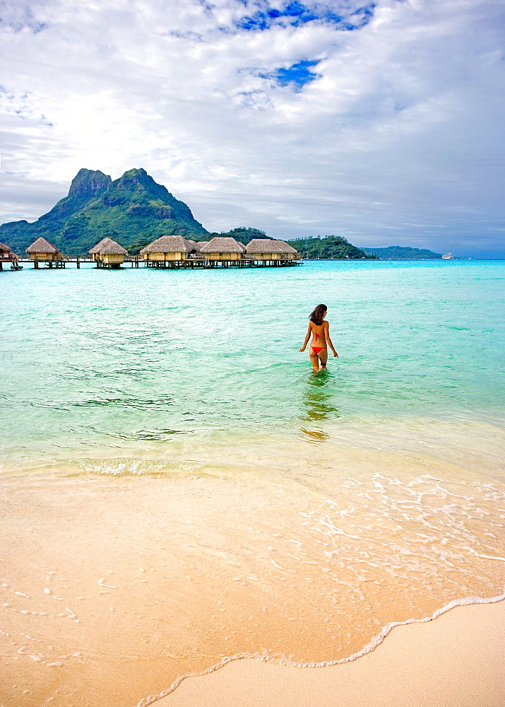 French Polynesia, Tahiti, Bora Bora, Woman in the ocean with bungalows in the background.