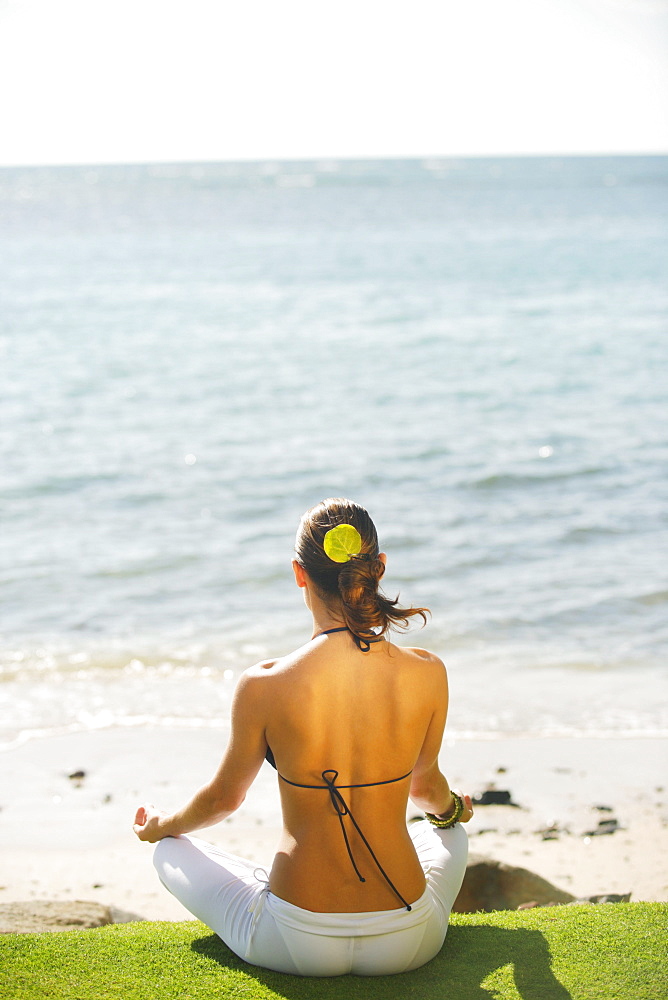 Hawaii, Woman meditating on grass near ocean, View from behind.