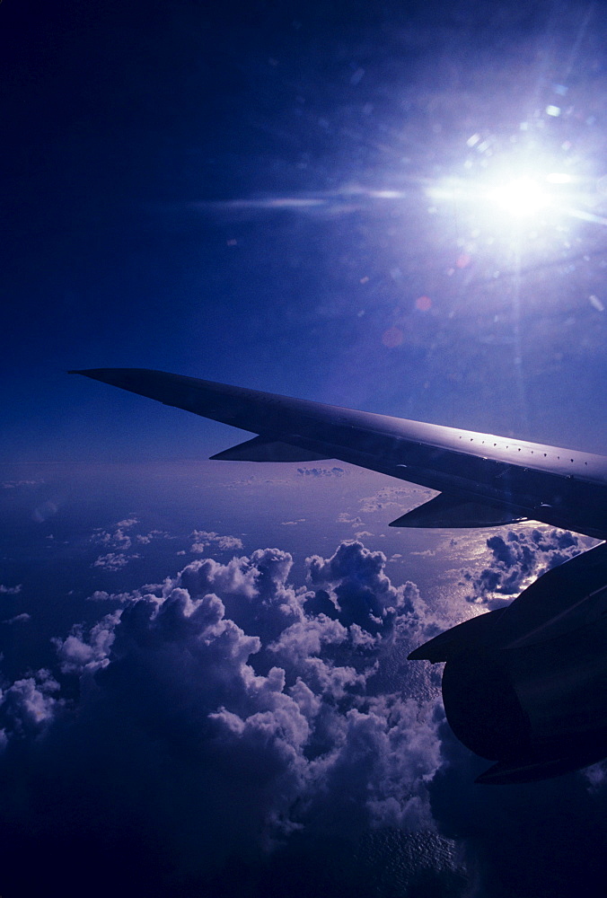 View of sun sky and clouds from window of airplane, wing in view.