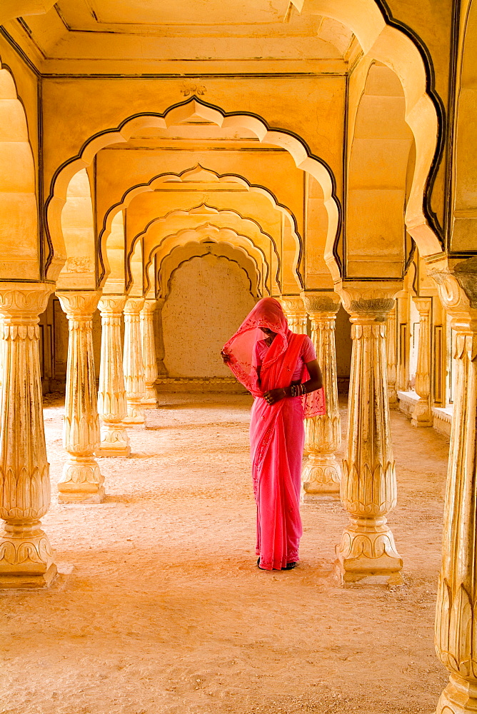 India, Rajasthan, Jaipur, Amber Fort Temple, woman in bright pink sari stands beneath arches.