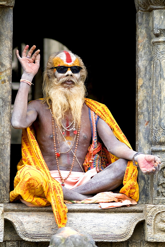 Nepal, Kathmandu, painted religious man wearing western sunglasses at Pashupatinath holy Hindu place on Bagmati River.