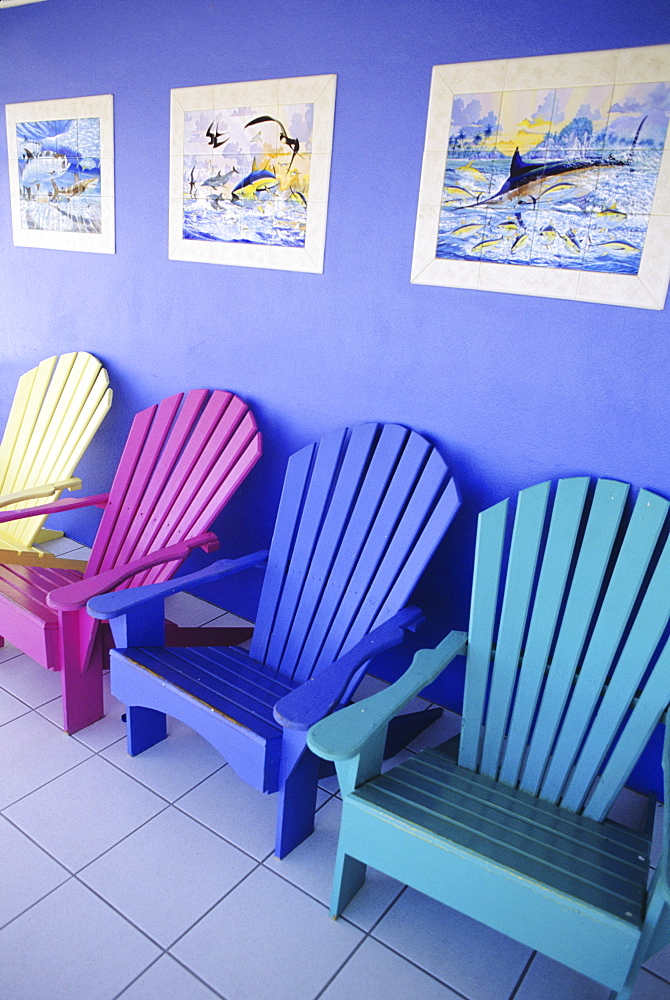 Cayman Islands, Grand Cayman, Colorful wooden chairs and artwork on storefront.