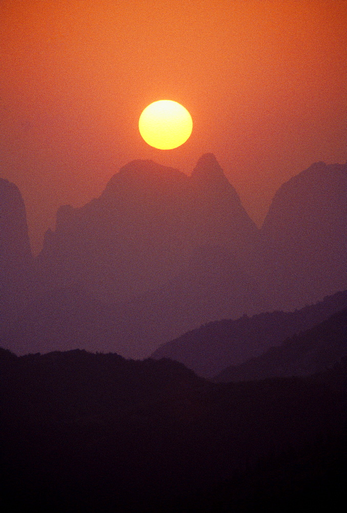 China, Guilin, golden sunball over Piled Silk Mountains, orange and pink misty sunset