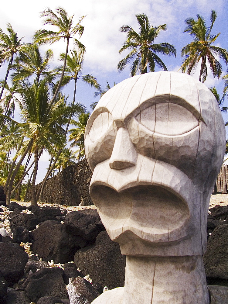 Hawaii, Big Island, Puuhonua O Honaunau, City of Refuge, Ki'i against blue sky and palm trees.