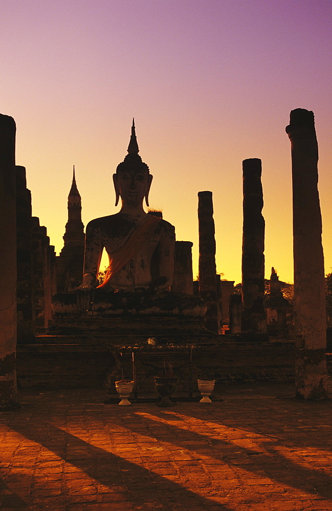 Thailand, Sukhothai, Wat Mahathat, Buddha and pillars backlit at sunset