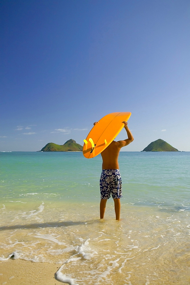 Surfer walking into the water from the beach with board over his head.