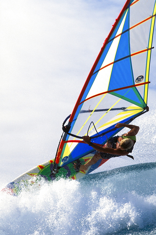 Close-up angle view of Josh Angulo over tip of wave, pale blue sky in background