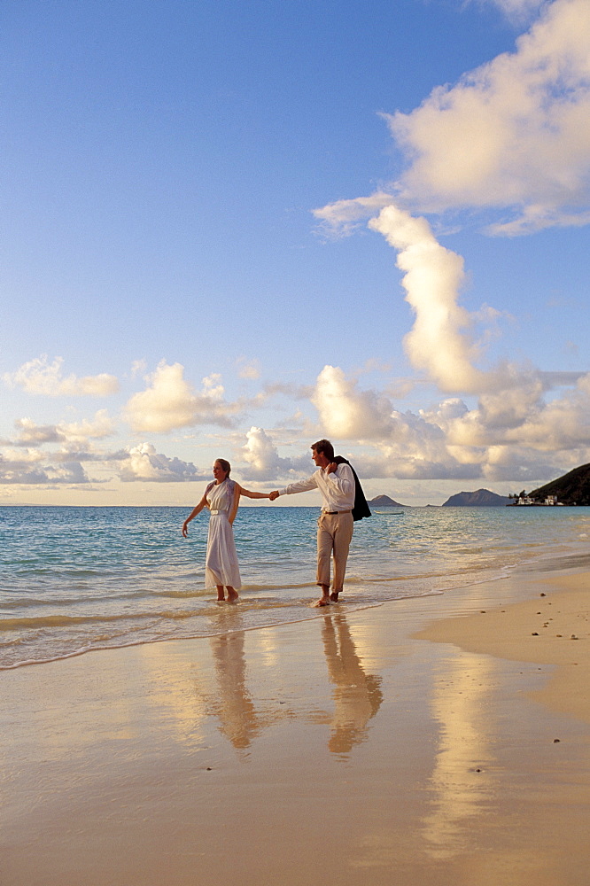 Hawaii, Romantic couple walk along shoreline at sunset