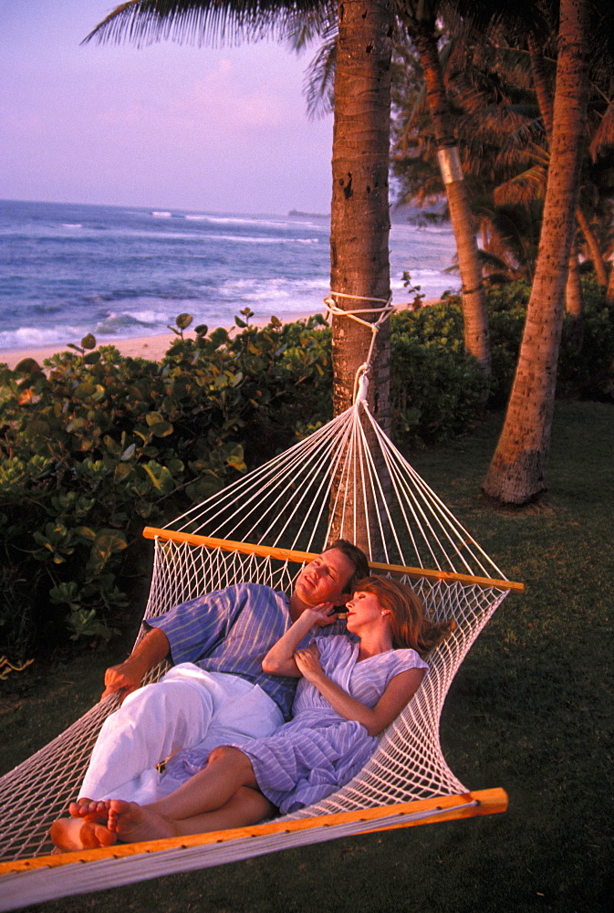 Couple at sunset, relaxing in Hammock in tropical setting. Hawaii