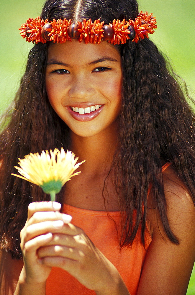 Young Hawaiian girl with orange haku holding flower.