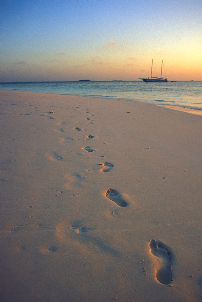 Footprints in white sand along shoreline at sunset