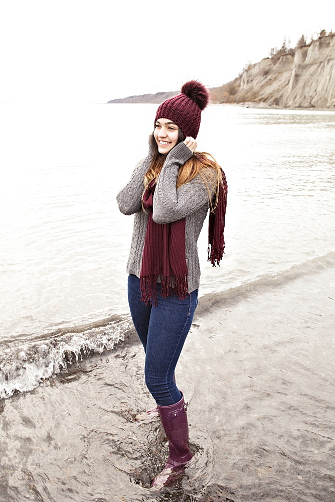 Girl standing in shallow water in autumn at the Scarborough Bluffs wearing a knit hat and scarf, Toronto, Ontario, Canada