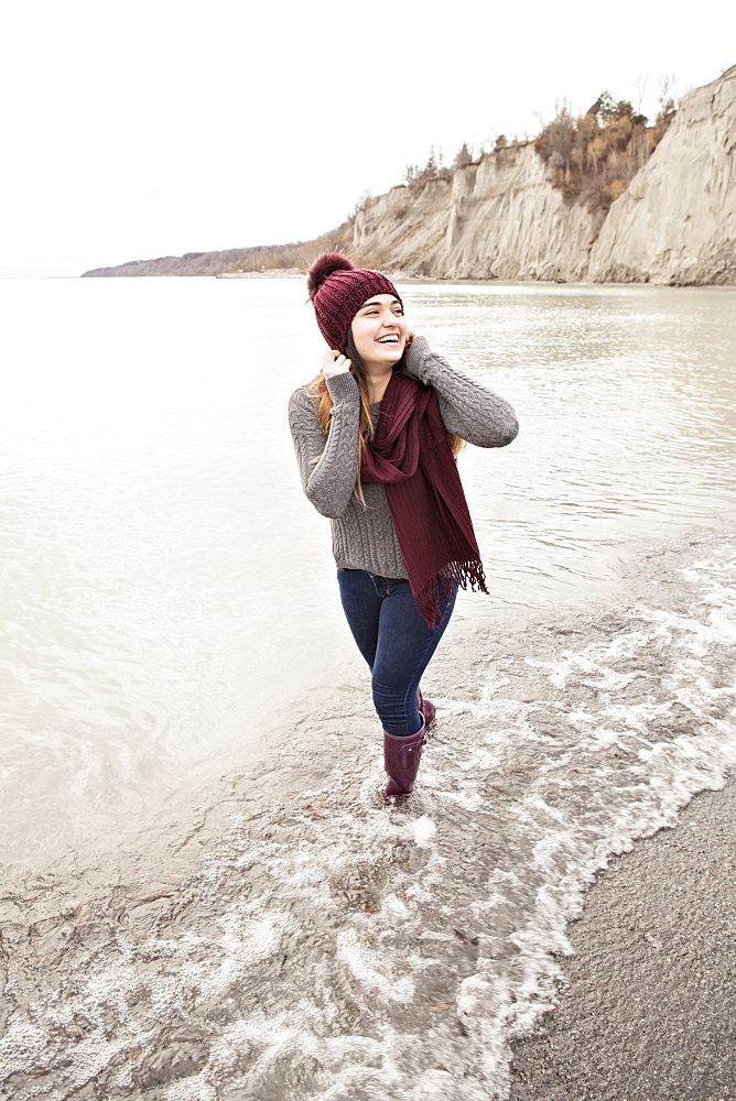 Girl standing in shallow water in autumn at the Scarborough Bluffs wearing a knit hat and scarf, Toronto, Ontario, Canada