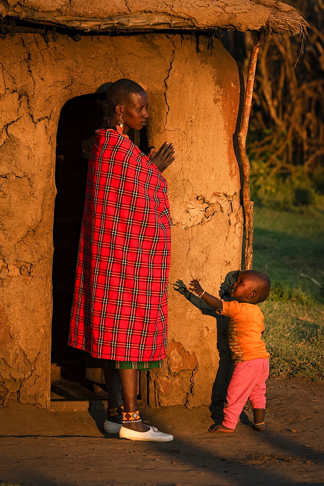 Woman in shuka with child outside hut, Tanzania