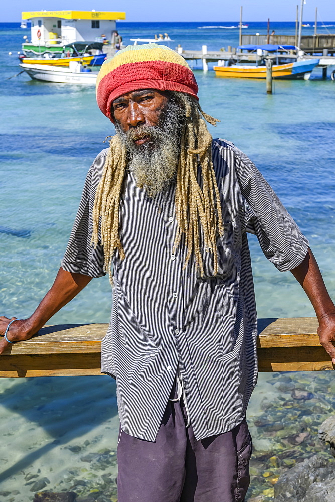 A man stands along the water's edge posing for the camera with boats moored at the dock in the background, depicting the people and lifestyle on the island of Roatan, West End Village, Roatan, Bay Islands Department, Honduras