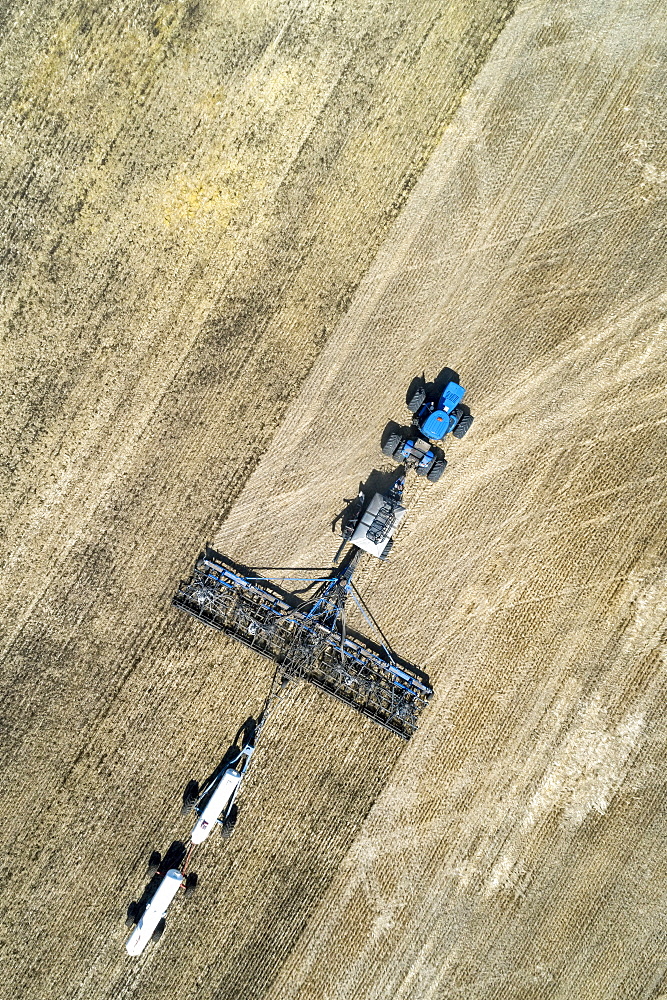 Aerial view of air seeder in field with white ammonia tanks, near Beiseker, Alberta, Canada