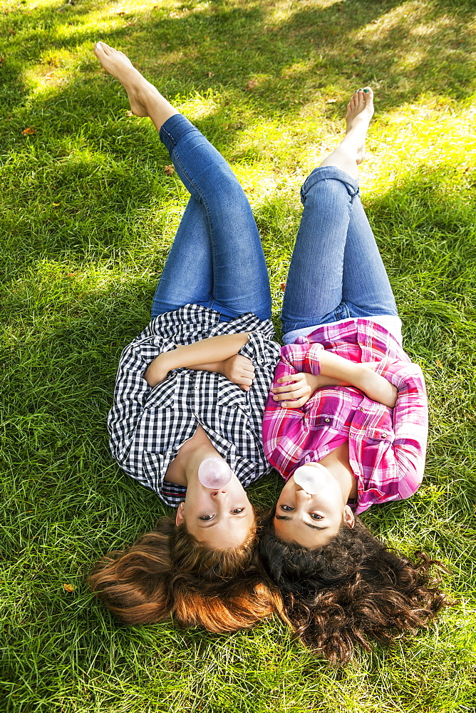 Two friends laying side by side on the grass blowing bubbles with bubblegum, Toronto, Ontario, Canada