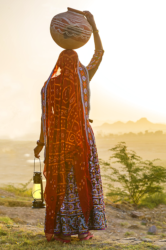 Ahir Woman in traditional colorful cloth carrying water in a clay jug on her head, Great Rann of Kutch Desert, Gujarat, India, Asia