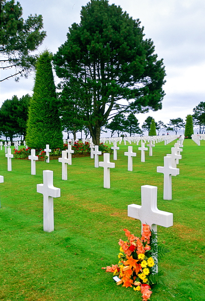 Headstones at a United States Military Cemetery at Utah Beach in Normandy, France.  Flowers have been left beside one of the crosses.