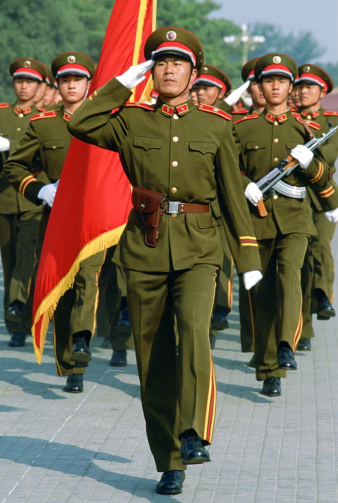 Soldiers salute while marching in Tiananmen Square with a red flag in Beijing (Peking), China