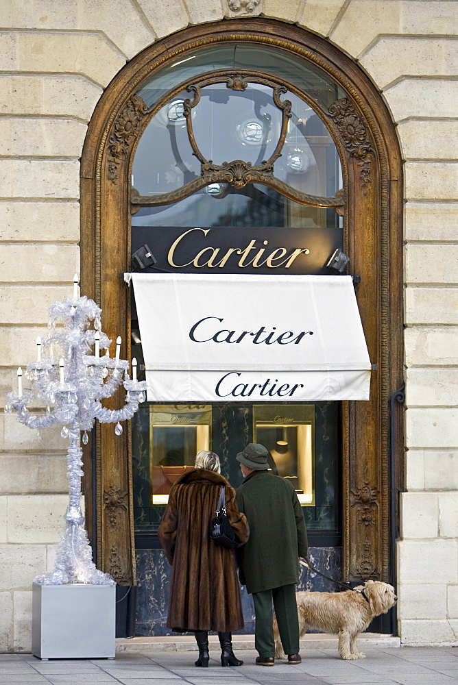 Stylish couple with dog look in Cartier shop window in Place Vendome, Central Paris, France