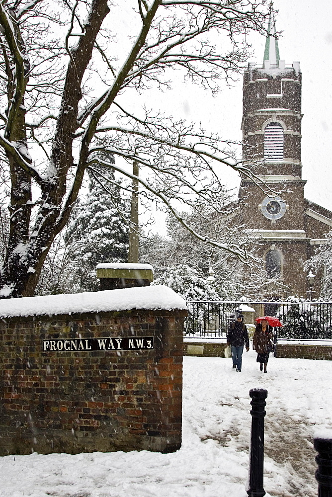 Two people walk by St John At Hampstead Parish Church and graveyard, North London, UK