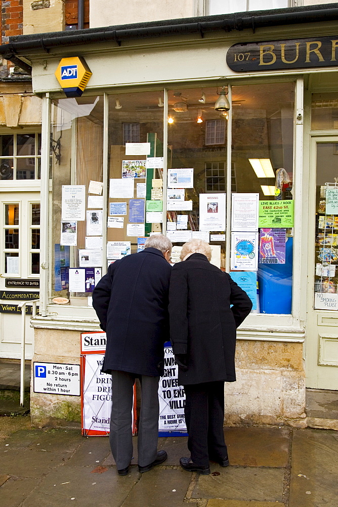 Couple browse the window of a newsagent's shop at Burford in the Cotswolds, United Kingdom