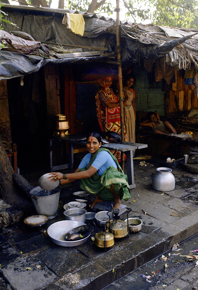 Woman cleans pots and pans at her makeshift homeon the street in Delhi, India.