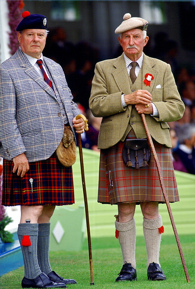 Two traditional Scotsmen wearing tartan kilts, tweed jackets, caps, sporrans and holding walking sticks at the Braemar Games, a Royal Highland gathering.