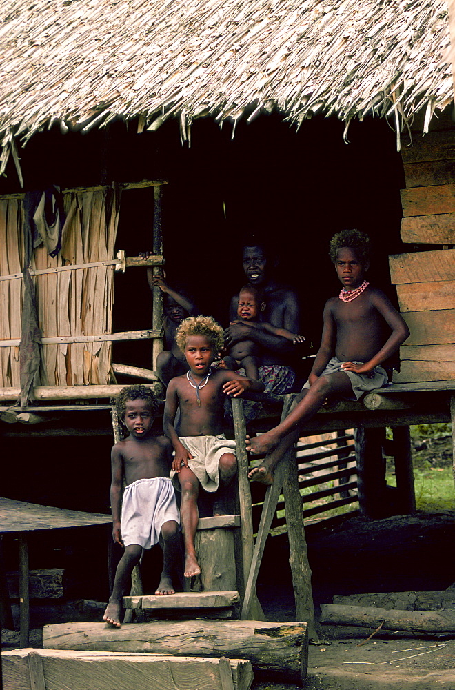 Mother and children at their traditional wood and straw roofed home in the Solomon Isles.