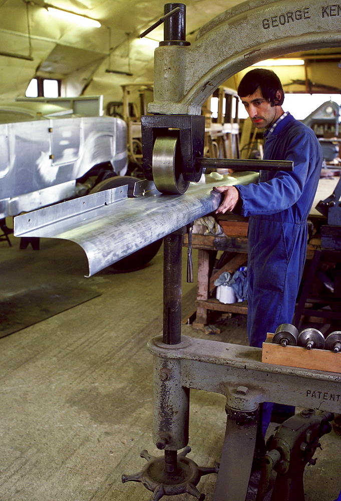 Man rolling an aluminium panel during the restoration of a rare vintage Rolls Royce, Gloucestershire, UK.