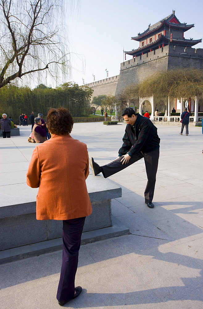 People stretching before practising Tai chi as part of their morning exercise, in the park by the City Wall, Xian, China