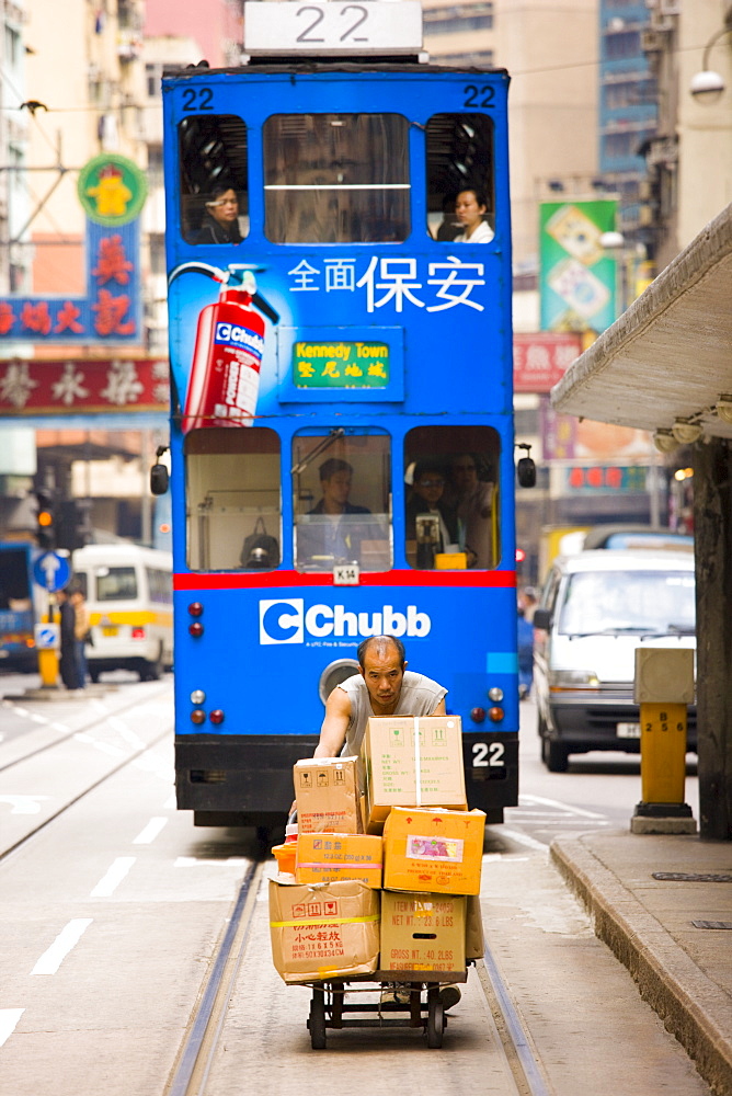 Tram behind man delivering food by trolley in old Chinese district, Des Voeux Road, Sheung Wan, Hong Kong, China