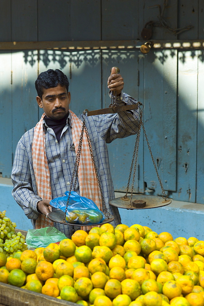 Indian man sells oranges at market stall in alleyway in the city of Varanasi, Benares, Northern India