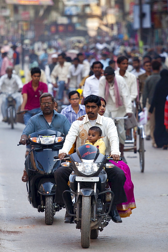 Fathers with children on cycles in crowded street scene during holy Festival of Shivaratri in city of Varanasi, Benares, Northern India