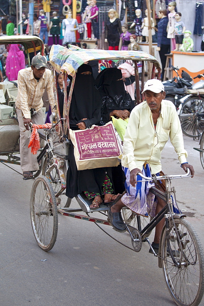 Muslim women travel by rickshaw in crowded street scene in city of Varanasi, Benares, Northern India