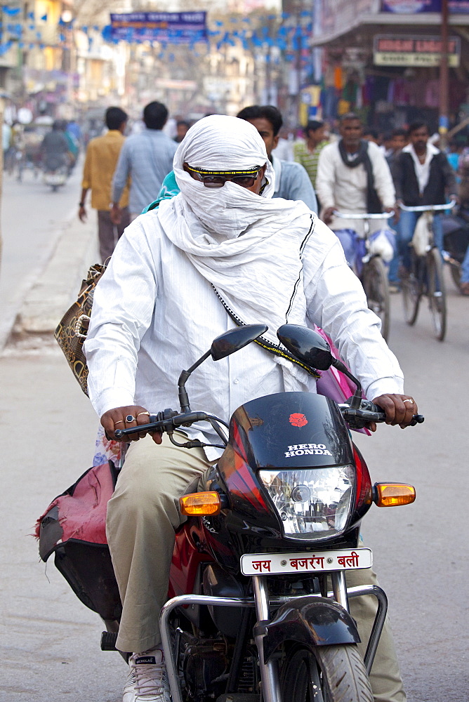 Man driving Hero Honda motorcycle with covered head and face in street scene in city of Varanasi, Benares, Northern India