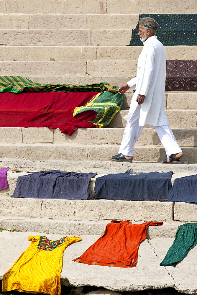 Indian man walks past laundry drying on the steps of Kali Ghat by the The Ganges River in City of Varanasi, Benares, India