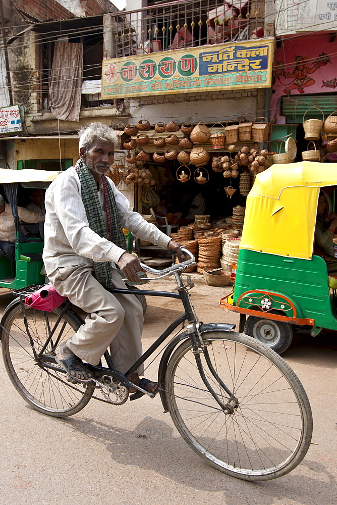 Indian man riding bicycle street scene in city of Varanasi, Benares, Northern India