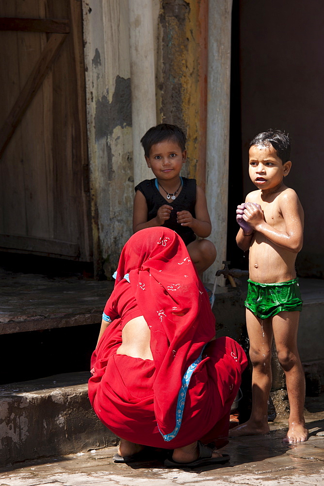 Indian children being bathed with water from a tap in the street by their mother in Agra, India