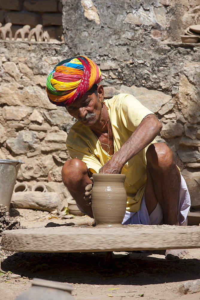 Indian potter in traditional Rajasthani turban works on potter's wheel at home making clay pots in Nimaj village, Rajasthan, Northern India