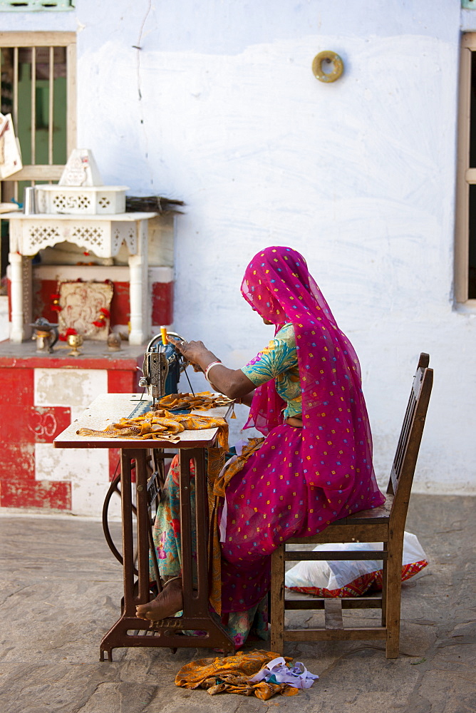 Indian woman wearing traditional Rajasthani sari works at home using sewing machine in village of Nimaj, Rajasthan, Northern India