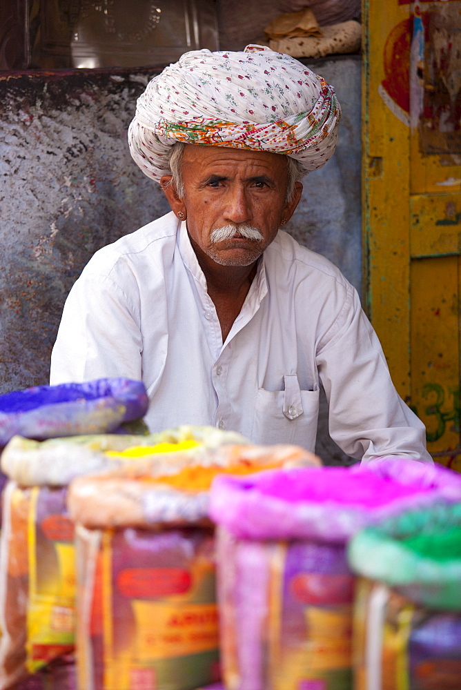 Indian man selling powder paint colours for Holi festival on sale at Katala Bazar in Jodhpur, Rajasthan, Northern India