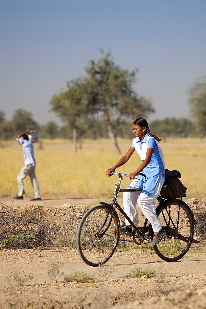 Young Indian girl in school uniform riding bicycle to her school near Rohet in Rajasthan, Northern India