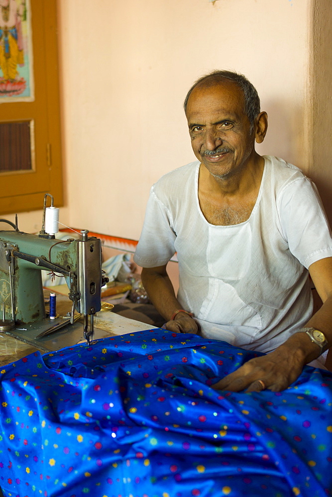 Indian man with traditional sewing machine making sari in Rajasthani colourful silk fabric in Narlai village in Rajasthan, Northern India