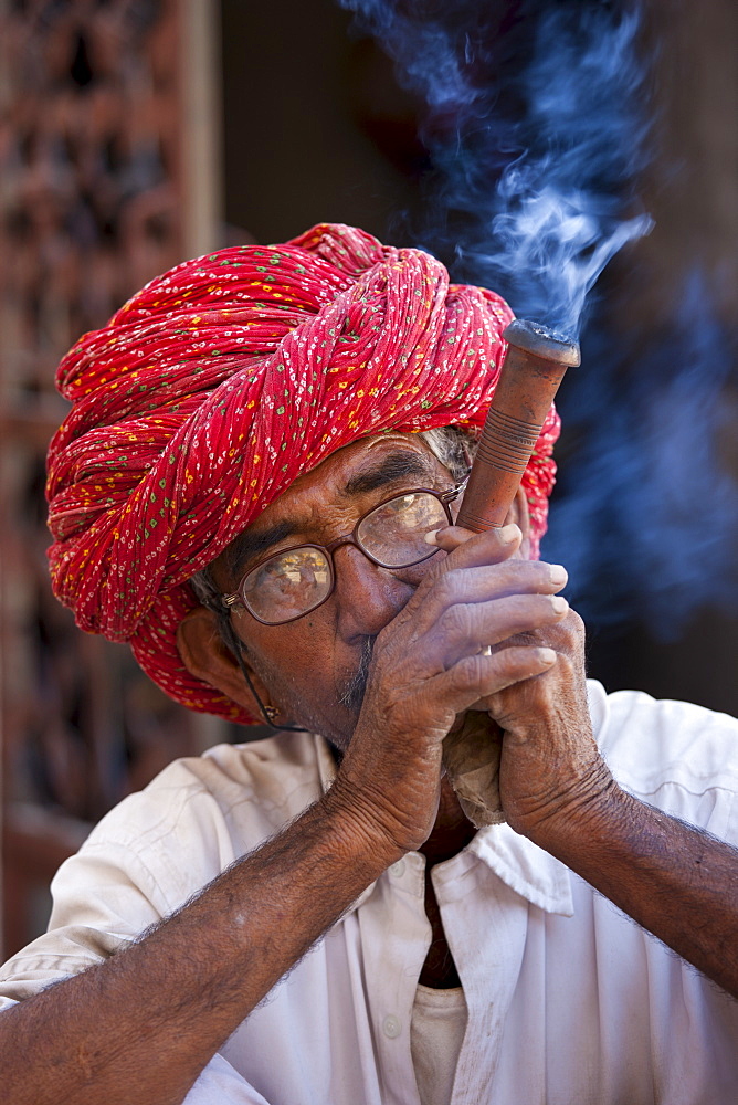 Indian man wearing Rajasthani turban smokes traditional clay pipe in Narlai village in Rajasthan, Northern India