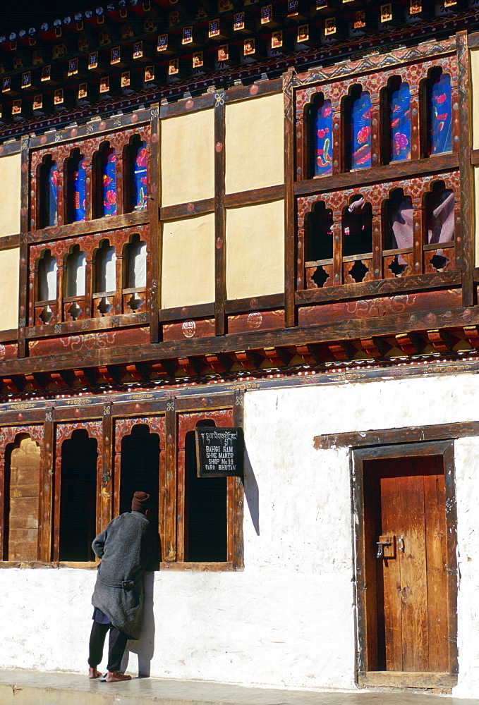 Bhutanese man removes his shoes as he leans in the open carved window of the Shoe Shop in Paro, Bhutan