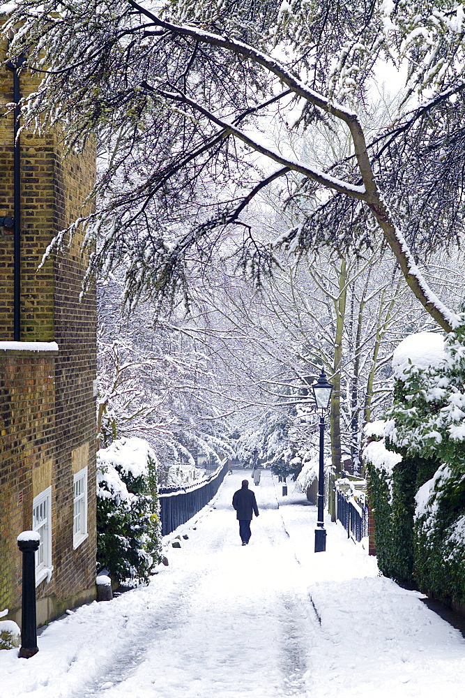 Lone figure walks through deep snow in Holly Place in leafy Hampstead, North London, United Kingdom