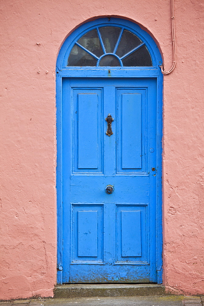 Bright  blue Georgian style door with fanlight above and pink lime mortar wall, in Ardmore Village, County Waterford, Ireland