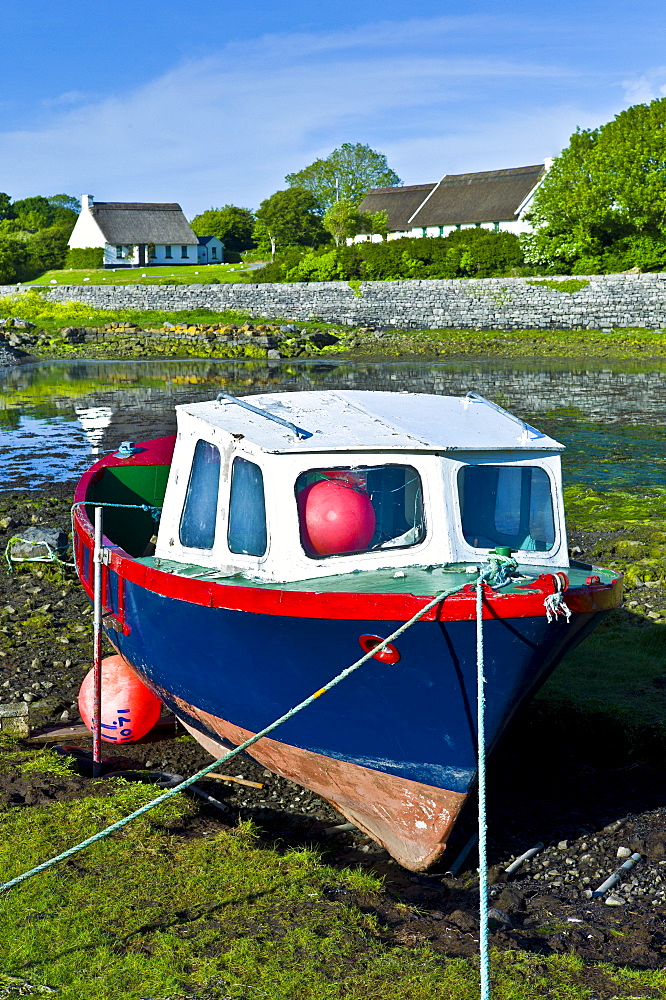 Brightly coloured fishing boat in the quay and thatched cottages  at Ballyvaughan, County Clare, West of Ireland